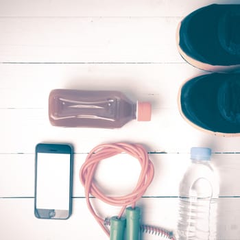 fitness equipment : running shoes,jumping rope,water,juice and phone on white wood background vintage style