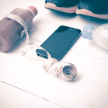 fitness equipment:running shoes,measuring tape,water,juice and phone on white wood background vintage style