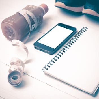 fitness equipment:running shoes,juice,measuring tape,notepad and phone on white wood background vintage style