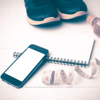 fitness equipment:running shoes,juice,measuring tape,notepad and phone on white wood background vintage style