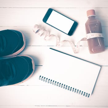 fitness equipment:running shoes,juice,measuring tape,notepad and phone on white wood background vintage style