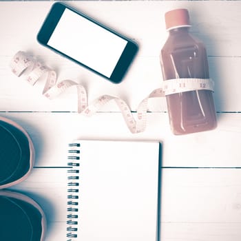 fitness equipment:running shoes,juice,measuring tape,notepad and phone on white wood background vintage style