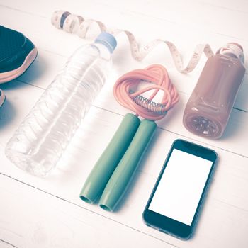 fitness equipment:running shoes,phone,measuring tape,water,juice and jumpong rope on white wood background vintage style