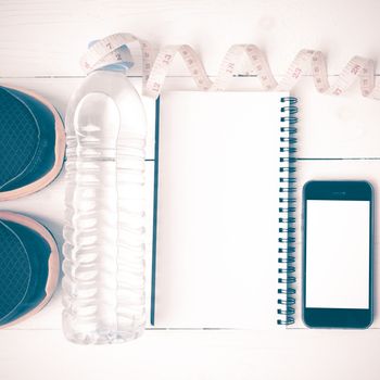 fitness equipment:running shoes,water,measuring tape,notepad,phone and juice on white wood background vintage style