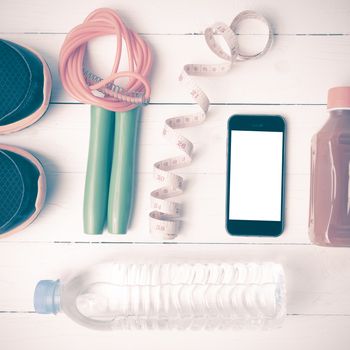 fitness equipment:running shoes,phone,measuring tape,water,juice and jumpong rope on white wood background vintage style