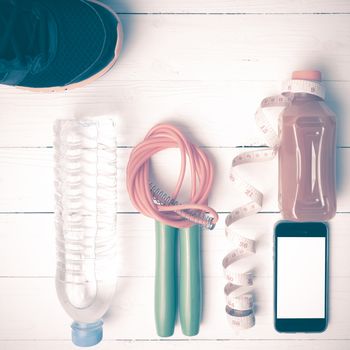 fitness equipment:running shoes,phone,measuring tape,water,juice and jumpong rope on white wood background vintage style