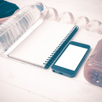 fitness equipment:running shoes,water,measuring tape,notepad,phone and juice on white wood background vintage style