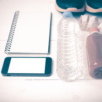 fitness equipment:running shoes,water,measuring tape,notepad,phone and juice on white wood background vintage style