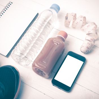 fitness equipment:running shoes,water,measuring tape,notepad,phone and juice on white wood background vintage style