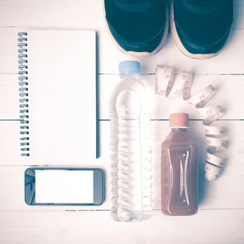 fitness equipment:running shoes,water,measuring tape,notepad,phone and juice on white wood background vintage style