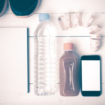 fitness equipment:running shoes,water,measuring tape,notepad,phone and juice on white wood background vintage style