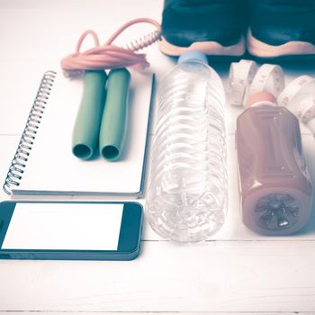 fitness equipment:running shoes,jumping rope,notepad,phone,water,juice and measuring tape on white wood background vintage style