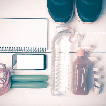 fitness equipment:running shoes,jumping rope,notepad,phone,water,juice and measuring tape on white wood background vintage style