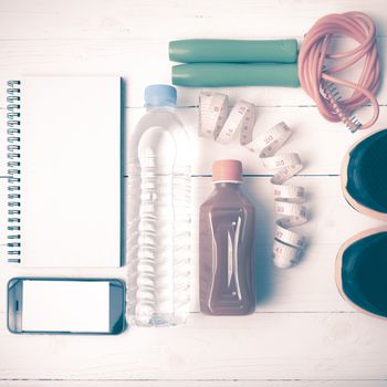 fitness equipment:running shoes,jumping rope,notepad,phone,water,juice and measuring tape on white wood background vintage style