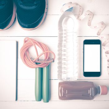 fitness equipment:running shoes,jumping rope,notepad,phone,water,juice and measuring tape on white wood background vintage style