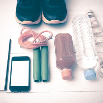 fitness equipment:running shoes,jumping rope,notepad,phone,water,juice and measuring tape on white wood background vintage style