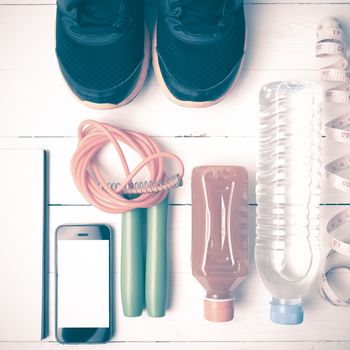 fitness equipment:running shoes,jumping rope,notepad,phone,water,juice and measuring tape on white wood background vintage style