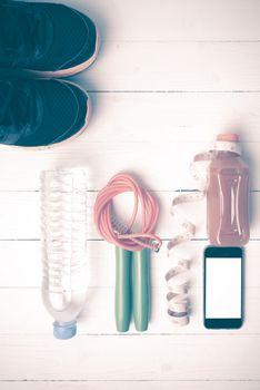 fitness equipment:running shoes,phone,measuring tape,water,juice and jumpong rope on white wood background vintage style