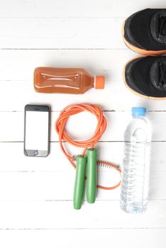 fitness equipment : running shoes,jumping rope,water,juice and phone on white wood background
