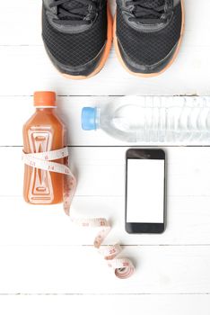 fitness equipment:running shoes,measuring tape,water,juice and phone on white wood background