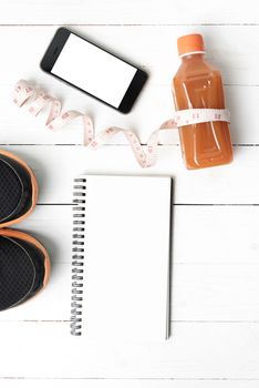 fitness equipment:running shoes,juice,measuring tape,notepad and phone on white wood background