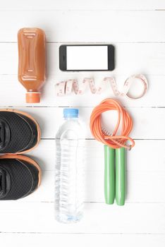fitness equipment:running shoes,phone,measuring tape,water,juice and jumpong rope on white wood background