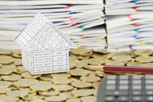Brown pencil and house on stack of gold coins have blur calculator and pile of document as foreground and background.