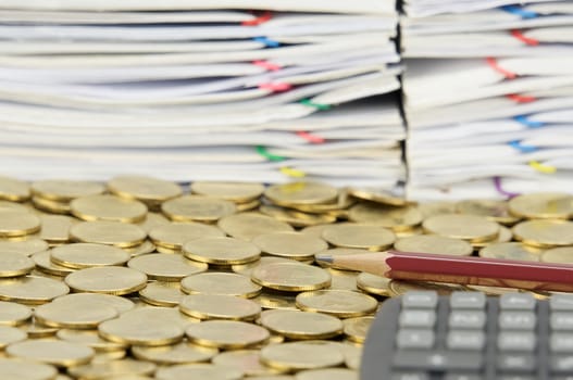 Brown pencil on stack of gold coins have blur calculator and pile of document as foreground and background.