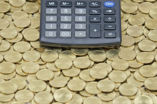 Black calculator on stack of gold coins as gold background. 