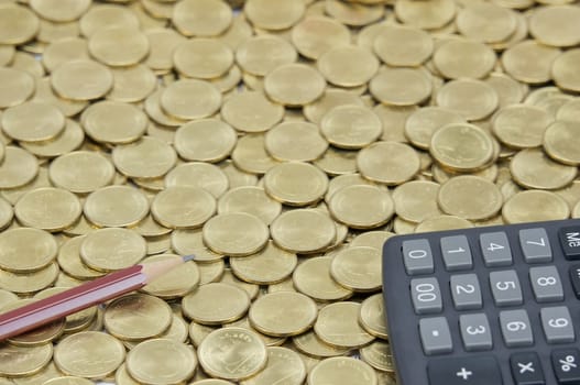 Brown pencil with black calculator on stack of gold coins as gold background. 