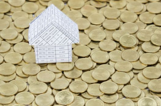 Paperwork as house on stack of gold coins as gold background. 