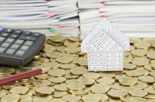 Pencil and calculator with house on stack of gold coins have pile of document as background.