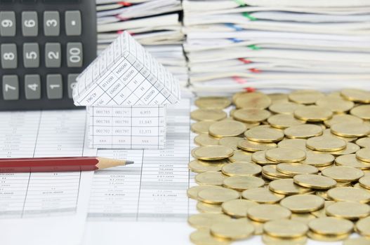 Pencil in front of house with stack of gold coins on another side on finance account have blur calculator place vertical and pile of document as background.