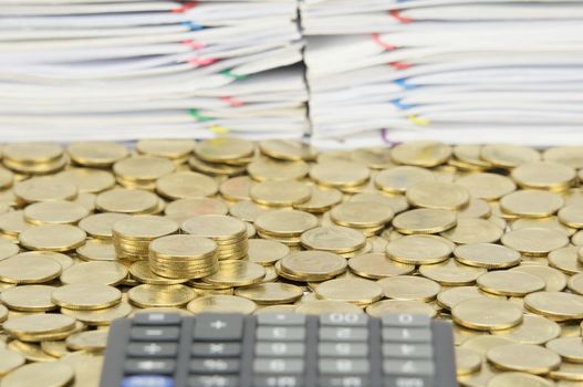 Pile of gold coins on stack of gold coins have blur calculator and pile of document as foreground and background.