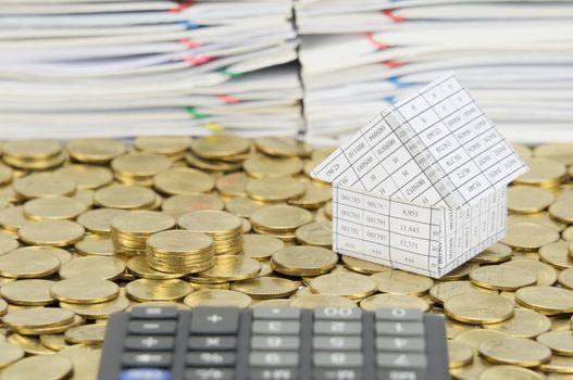 Pile of gold coins with house on stack of gold coins have blur calculator and pile of document as foreground and background.