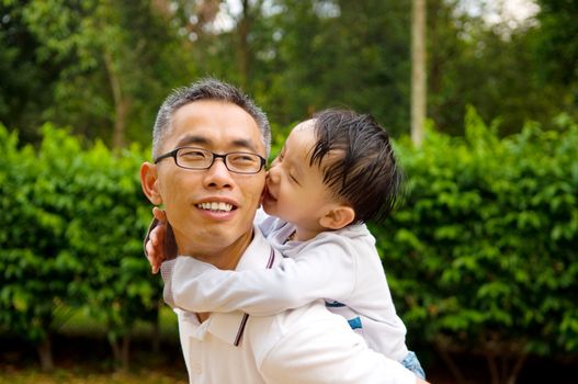 Asian father giving piggyback ride to his son in the evening sunshine