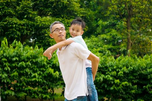 Asian father giving piggyback ride to his son in the evening sunshine