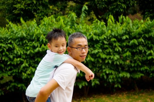 Asian father giving piggyback ride to his son in the evening sunshine