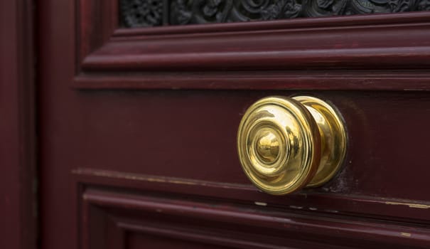 Shiny brass metal doorknob on maroon red wooden entrance door