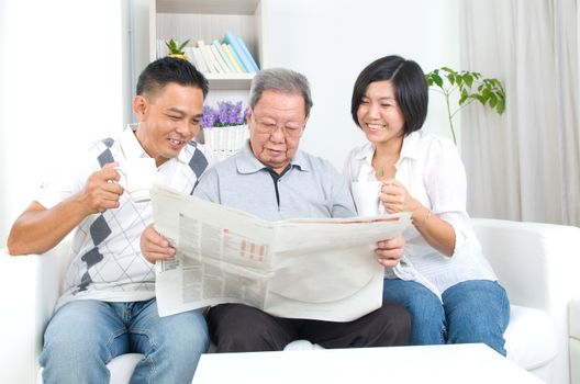 Portrait of chinese family reading newspaper together at home. Mature 80s senior man and his children.