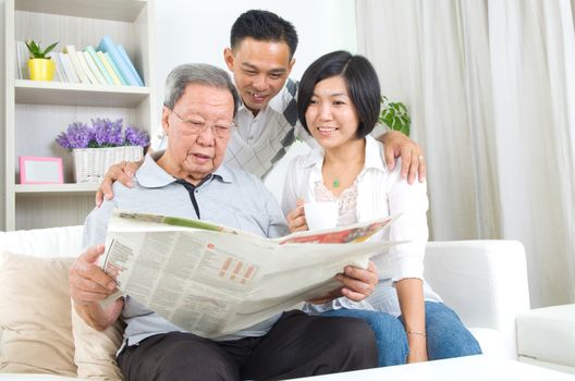 Portrait of chinese family reading newspaper together at home. Mature 80s senior man and his children.