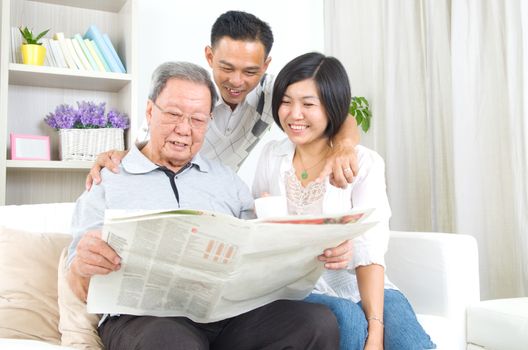 Portrait of chinese family reading newspaper together at home. Mature 80s senior man and his children.