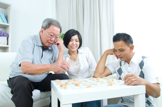 Chinese family playing Chinese chess at home, senior father with his  adult son and daughter.