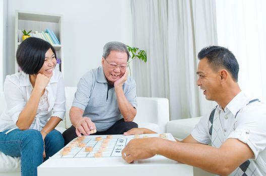 Chinese family playing Chinese chess at home, senior father with his  adult son and daughter.