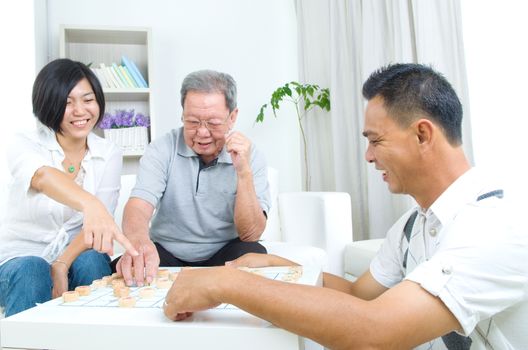 Chinese family playing Chinese chess at home, senior father with his  adult son and daughter.