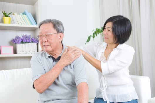 Asian old man shoulder pain, sitting on sofa , daughter massaging father shoulder. Chinese family, senior retiree indoors living lifestyle at home.