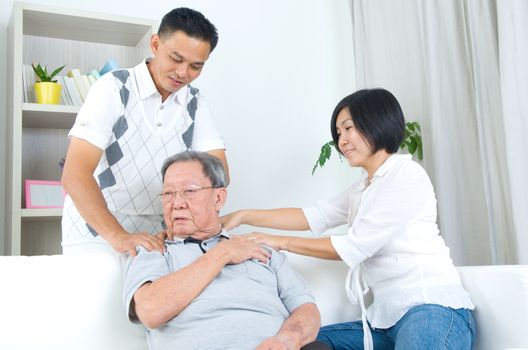 Asian old man shoulder pain, sitting on sofa , daughter and son massaging their father shoulder. Chinese family, senior retiree indoors living lifestyle at home.