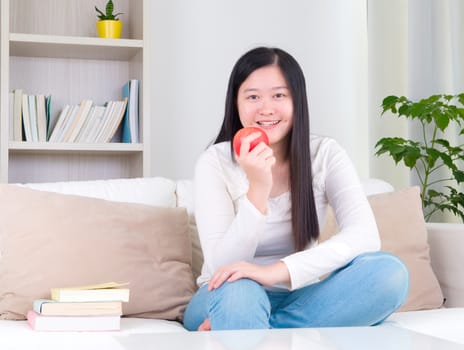 Happy Asian girl eating green apple. Young girl indoors living lifestyle at home.