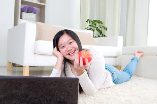 Portrait of attractive Asian girl using laptop and holding an apple. Young woman indoors living lifestyle at home.