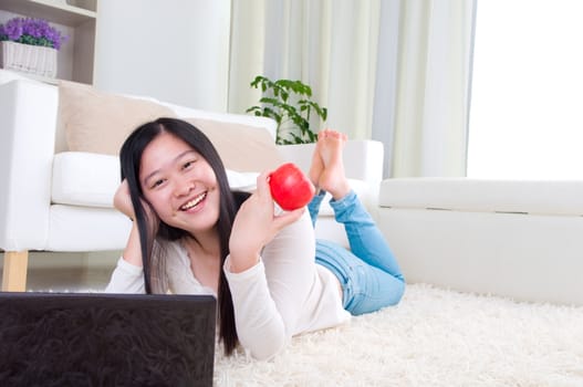 Portrait of attractive Asian girl using laptop and holding an apple. Young woman indoors living lifestyle at home.